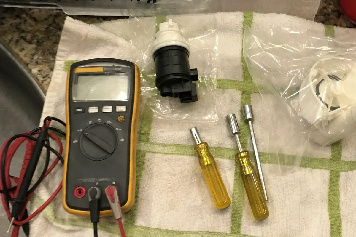 A bagged replacement blower motor on a folded towel beside a multimeter and two nut drivers