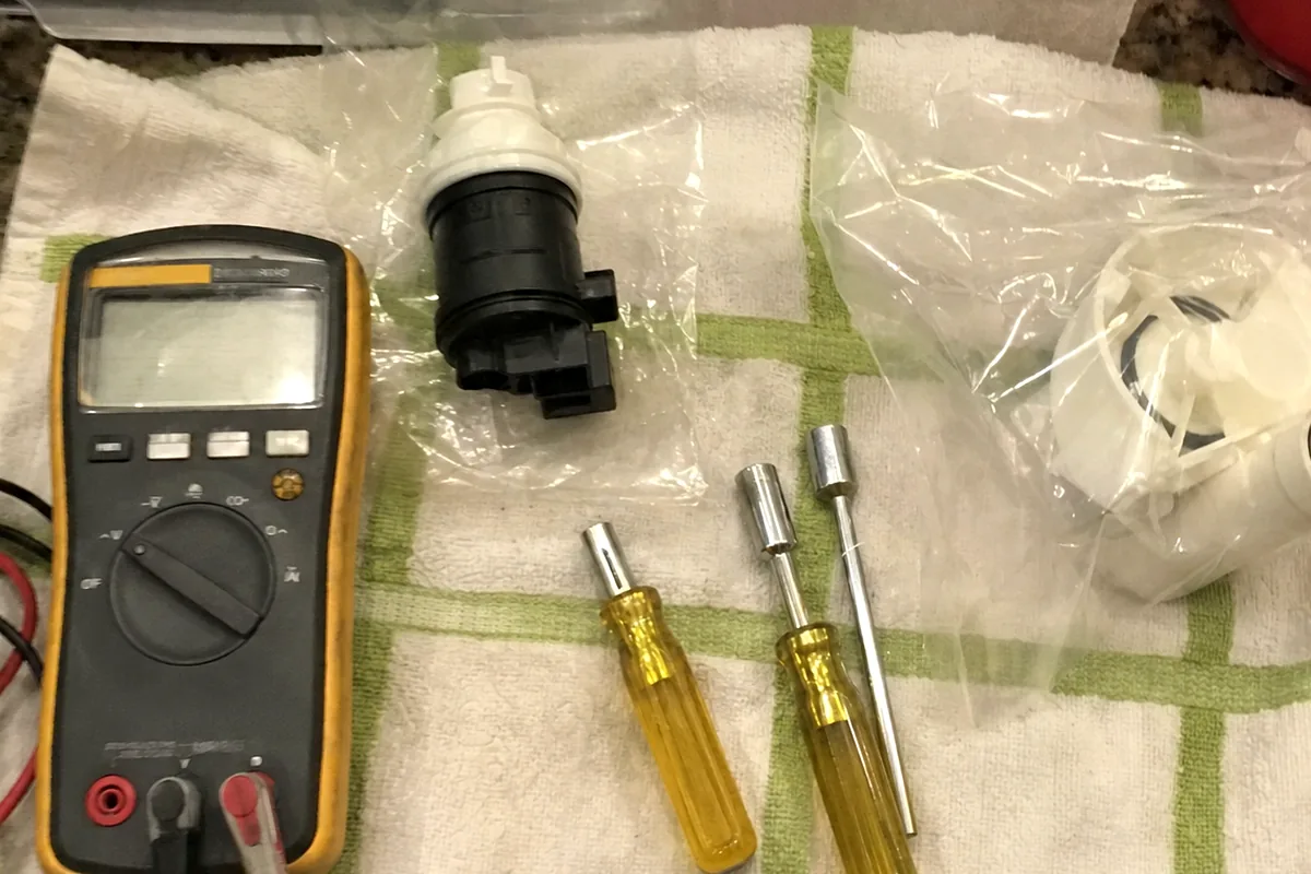 A blower motor still sealed in its bag laid beside a meter and screwdrivers on a work towel