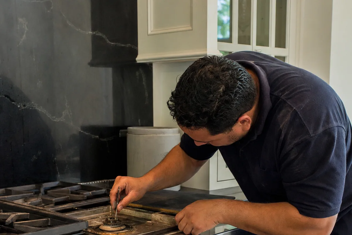 A hand steadying a burner cap on an all-gas range while the port ring underneath is checked