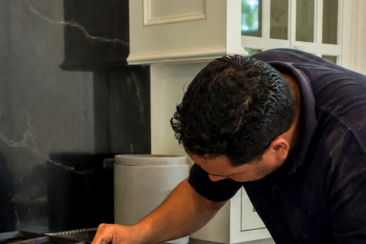 A range with its cast grates lifted off and a technician working at the exposed burner ring